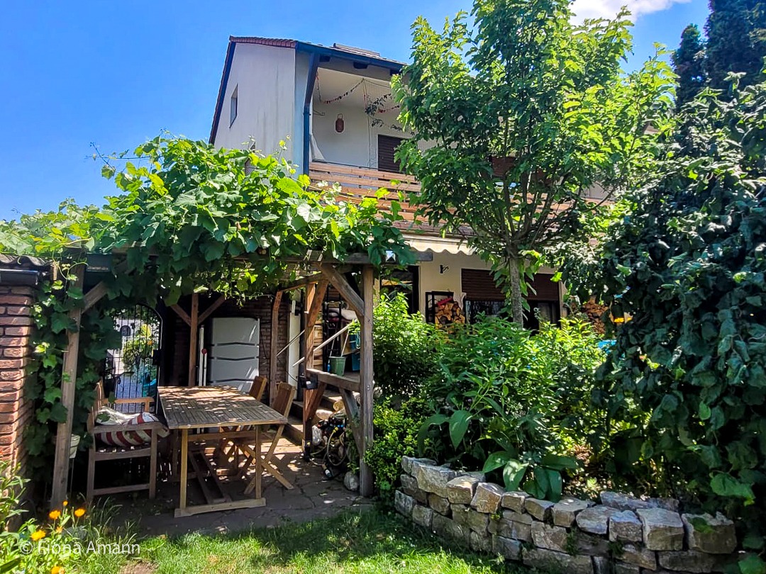 Eine Holz-Pergola steht zwischen Haus und Garten.